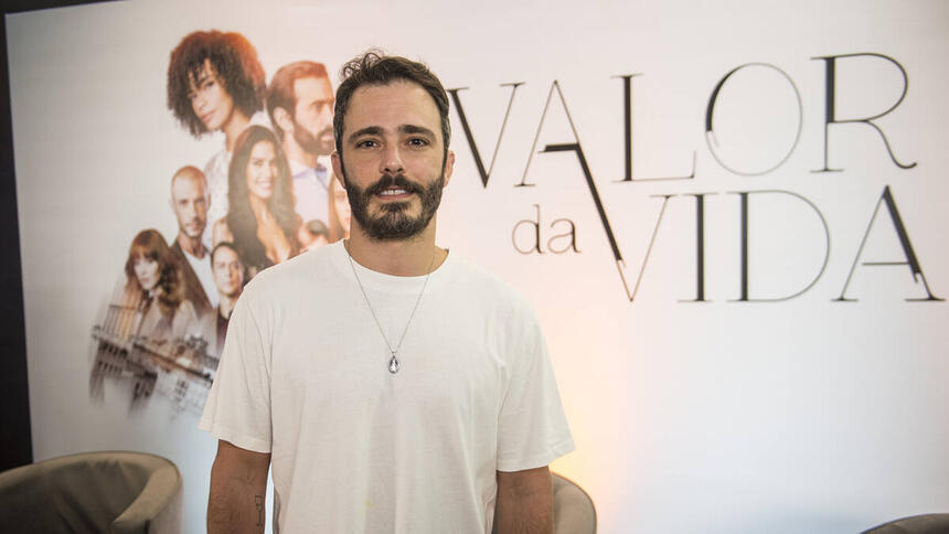 Ator Thiago Rodrigues em foto posada, na frente do banner de divulgação da novela Valor da Vida, na Band