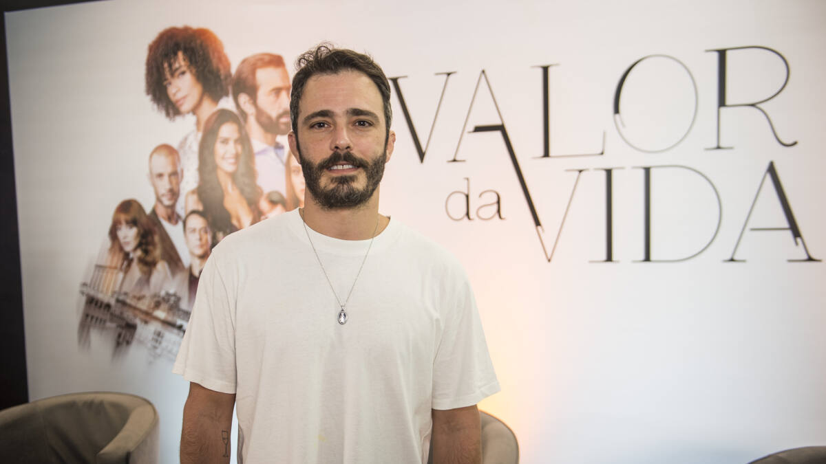 Ator Thiago Rodrigues em foto posada, na frente do banner de divulgação da novela Valor da Vida, na Band