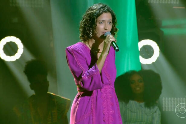 Adri Amorim com um vestido roxo, se apresentando no palco do The Voice Brasil 11