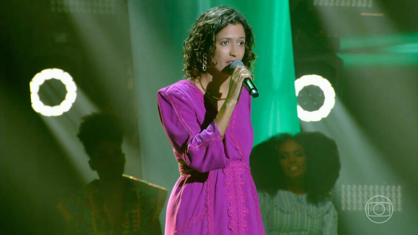Adri Amorim com um vestido roxo, se apresentando no palco do The Voice Brasil 11
