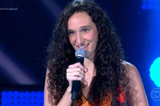 Antonia Medeiros cantando no palco do The Voice Brasil, com vestido florido e microfone na mão