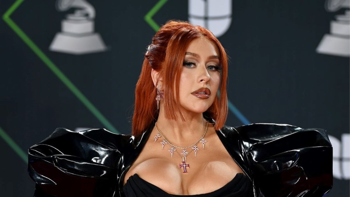 Christina Aguilera com look em ombreira preto, de couro, decotado, de cabelo preso, ruivo, olhando de lado, durante presença em premiação