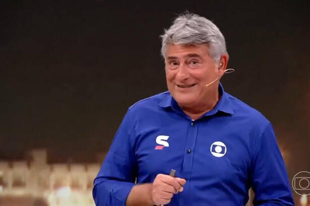 Cléber Machado com o uniforme azul de esporte da Globo, com um sorriso no rosto