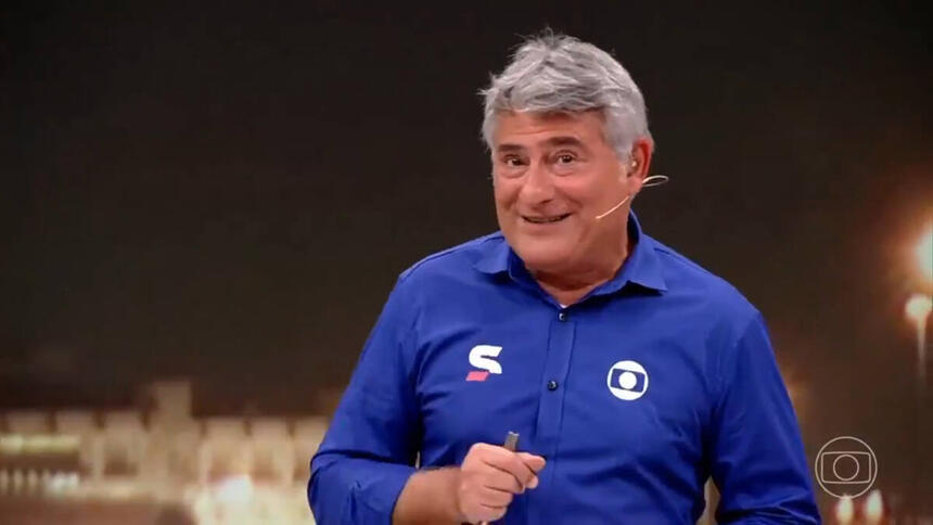 Cléber Machado com o uniforme azul de esporte da Globo, com um sorriso no rosto