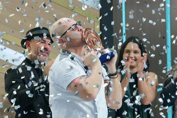 Diego erguendo o troféu de campeão do MasterChef Profissionais, em meio a chuva de papel picado