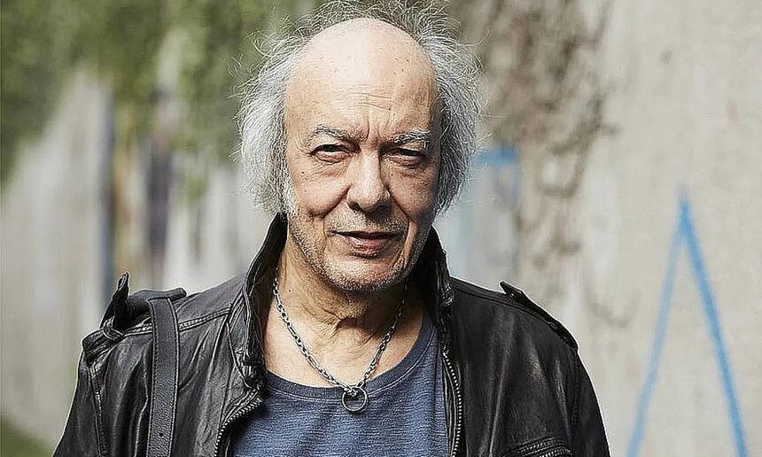 Erasmo Carlos de camisa azul marinho, jaqueta de couro preta, cabelos brancos, usando um colar de prata durante bastidores de gravação de filme