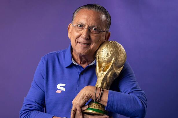 Galvão Bueno com o uniforme da equipe de esportes da Globo, segurando uma replica da taça da Copa do Mundo