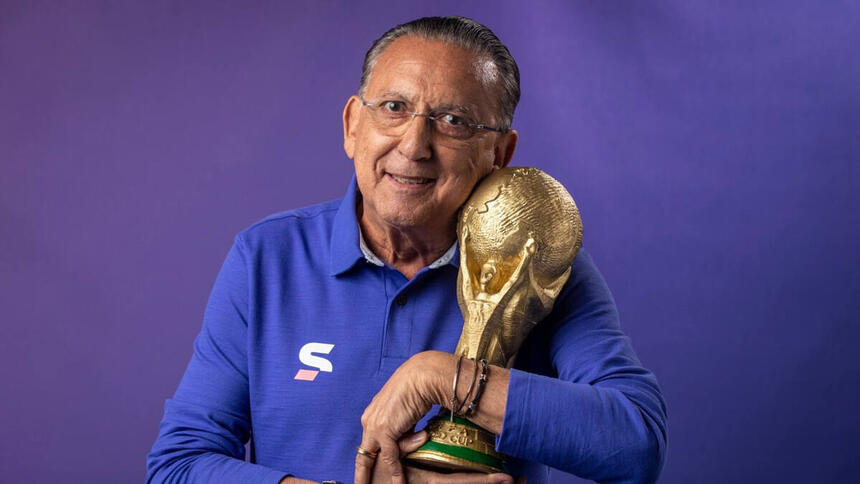 Galvão Bueno com o uniforme da equipe de esportes da Globo, segurando uma replica da taça da Copa do Mundo