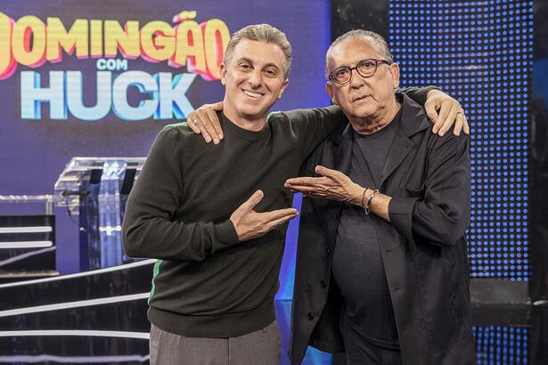 Luciano Huck e Galvão bueno de preto, apontando um ao outro com as mãos durante a gravação do 'Domingão', da TV Globo