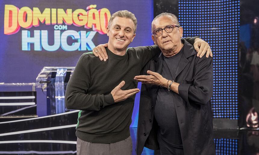 Luciano Huck e Galvão bueno de preto, apontando um ao outro com as mãos durante a gravação do 'Domingão', da TV Globo