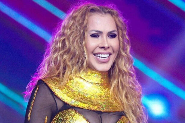 Joelma com um sorriso no rosto, vestindo uma roupa amarela com preto, em trecho de um show