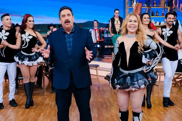 Joelma com look preto decotado, sorrindo, de bota ao lado de Ratinho durante gravação do programa no SBT