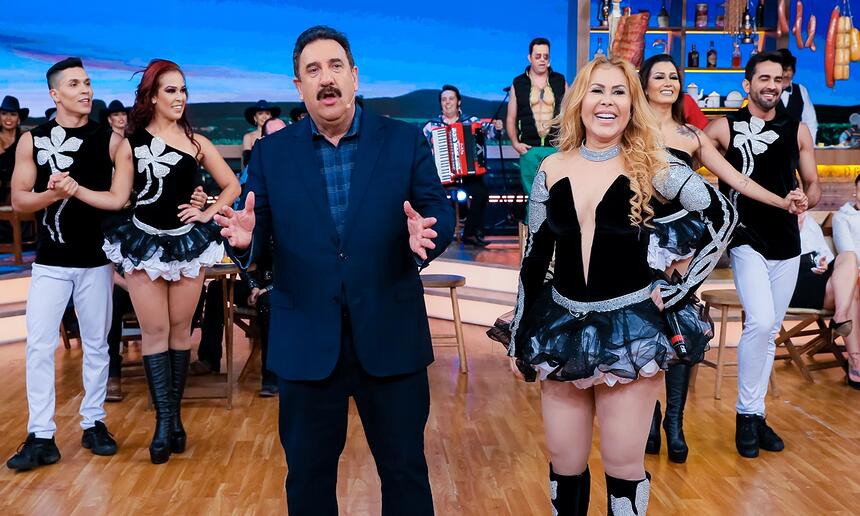 Joelma com look preto decotado, sorrindo, de bota ao lado de Ratinho durante gravação do programa no SBT