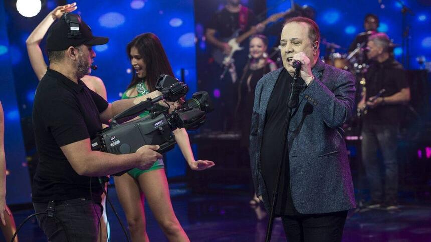 José Augusto de blazer e camisa preta, segurando o microfone durante performance no Faustão na Band