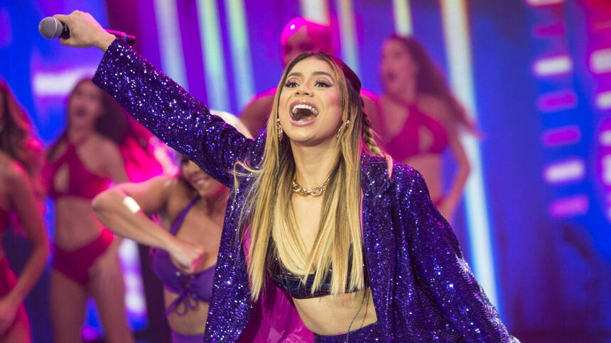 Lexa com o braço pra frente, sorrindo, com a boca aberta, durante gravação do Faustão na Band