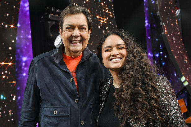 Luiza Martins de camisa preta sorrindo ao lado de Fausto Silva durante gravação do Faustão na Band