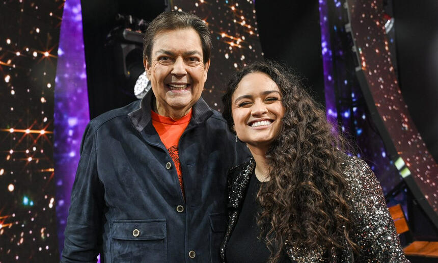 Luiza Martins de camisa preta sorrindo ao lado de Fausto Silva durante gravação do Faustão na Band