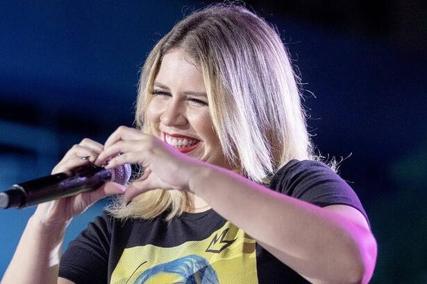 Marília Mendonça em trecho de um show fazendo um coração com as mãos