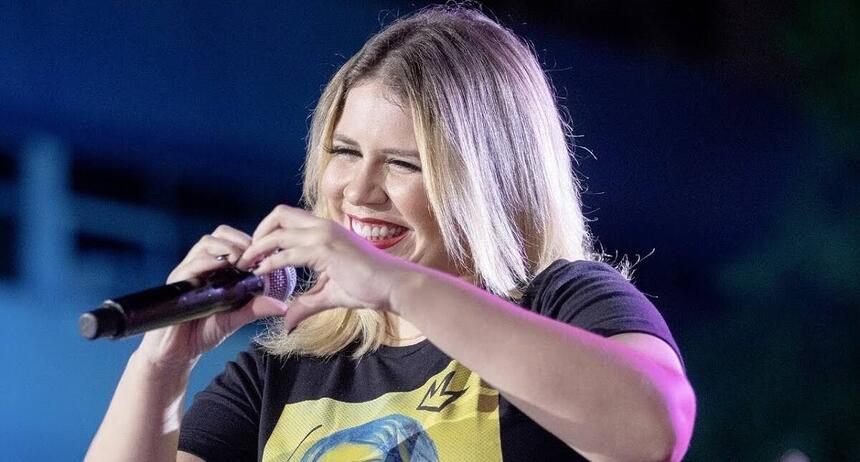 Marília Mendonça em trecho de um show fazendo um coração com as mãos