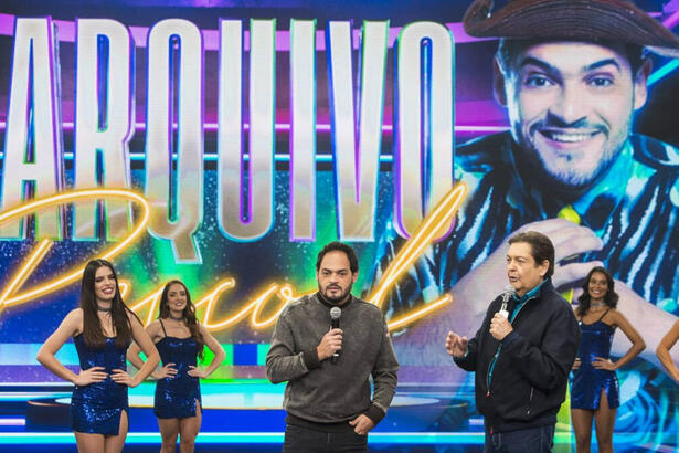 Faustão de jaqueta, camisa e calça preta ao lado de Matheus Cerá durante gravação do Faustão na Band