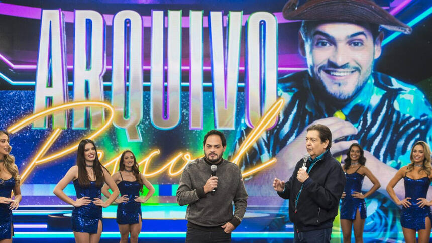 Faustão de jaqueta, camisa e calça preta ao lado de Matheus Cerá durante gravação do Faustão na Band