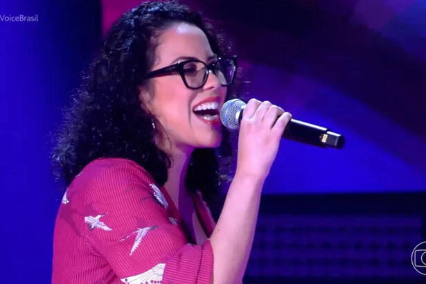 Mel fernandes com uma roupa rosa, cantando no palco do The Voice Brasil 11