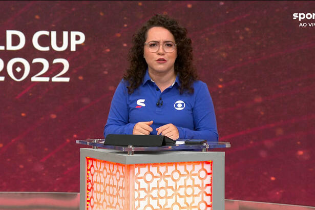 Natália Lara, com um uniforme de esporte da Globo, em frente ao púlpito, com um telão ao fundo