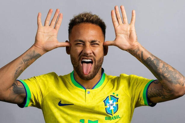 Neymar, com a camisa da Seleção Brasileira, fazendo careta, com a lígua para fora e com as duas próximas as orelhas