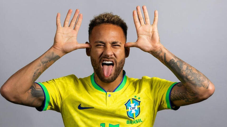 Neymar, com a camisa da Seleção Brasileira, fazendo careta, com a lígua para fora e com as duas próximas as orelhas