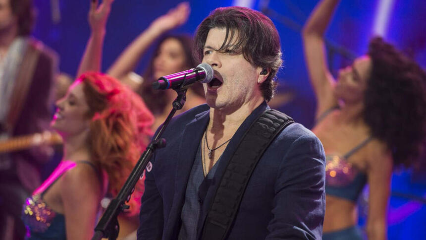 Paulo Ricardo de blazer e camisa preta, cantando durante gravação do Faustão na Band