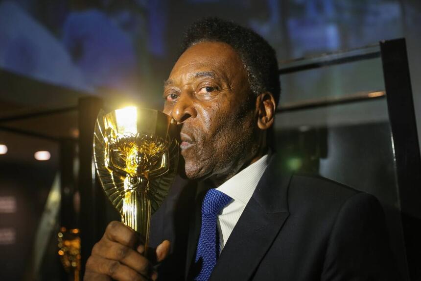 Pelé, com terno e gravata, segurando e beijando uma taça dourada