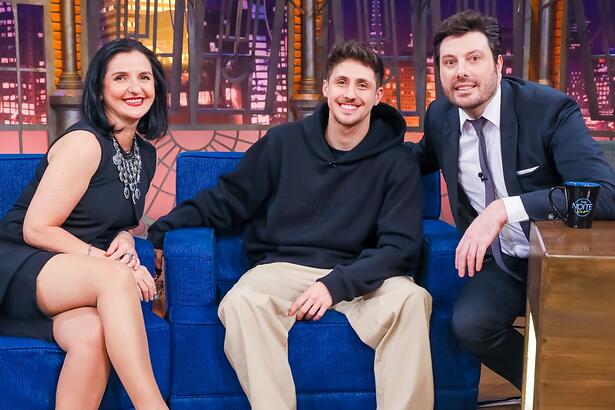 Pkllipe e Tuca de camisa preta, sorrindo, sentados num sofá azul ao lado de Danilo Gentili para gravação do The Noite, do SBT