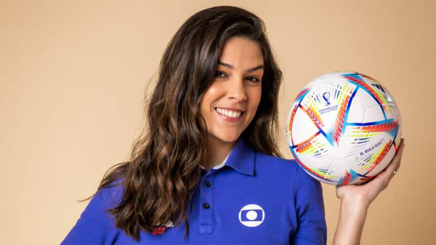 Renata Silveira com o uniforme de esporte da Globo, sorrindo e segurando uma bola na mão