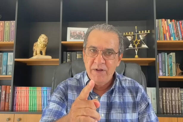 Silas Malafaia sentado, com camisa em xadrez azul e branca, usando óculos de grau, gesticulando durante vídeo