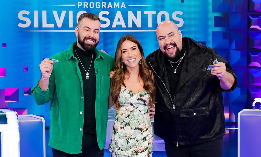 Fernando de jaqueta verde e camisa preta, sorrindo, ao lado esquerdo de Patricia Abravanel; Thiago Abravanel sorrindo ao lado direito de Patrícia durante gravação do Programa Silvio Santos, do SBT