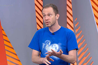 Tiago Leifert, com uma camisa azul nos estúdios do Globo Esprote, desticulando com as mãos e olhando para o seu lado direito