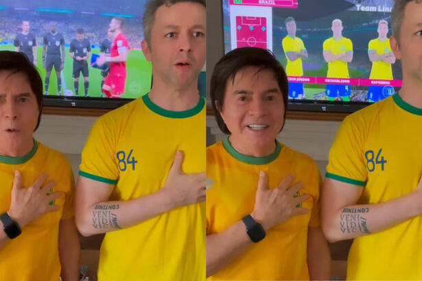 Xororó e Lucas Limas, com a blusa do Brasil e a mão no peito, cantando, com imagens do jogo do Brasil passando ao fundo em uma televisão