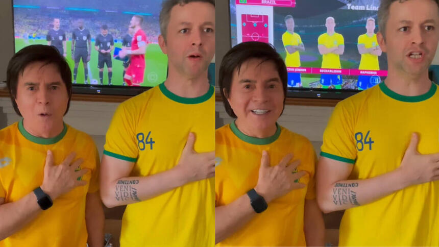 Xororó e Lucas Limas, com a blusa do Brasil e a mão no peito, cantando, com imagens do jogo do Brasil passando ao fundo em uma televisão