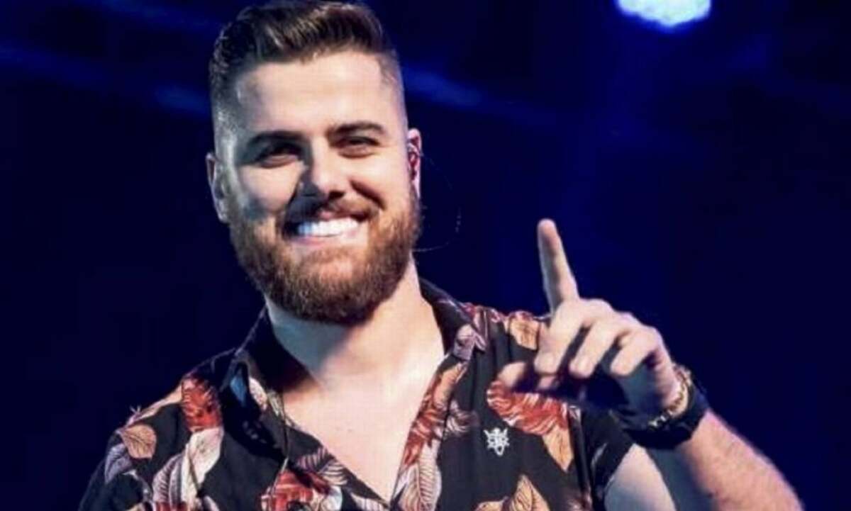 Zé Neto em trecho de um show, com sorriso aberto e apontando com o dedo