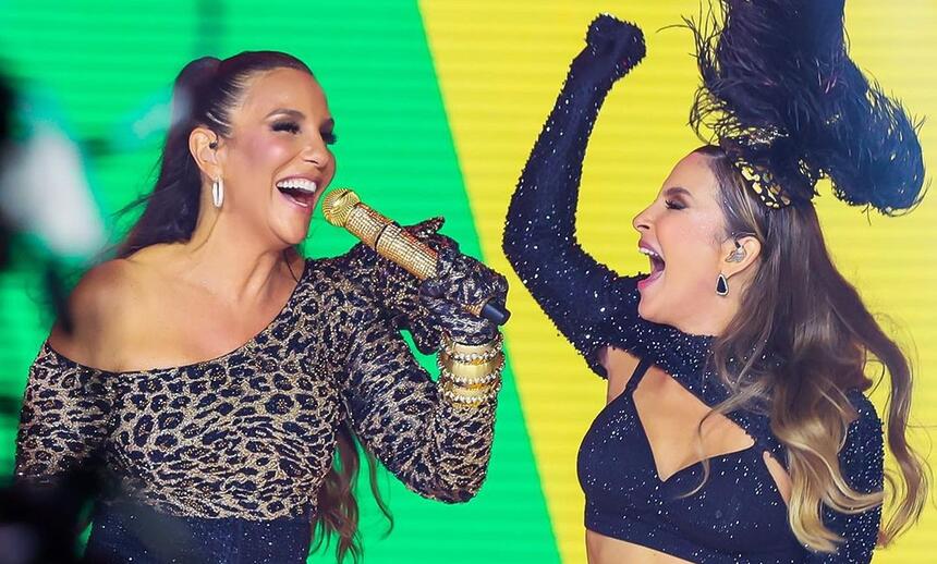 Claudia Leitte com o braço levantado, usando luva e top preto ao lado de Ivete Sangalo com look de onça e short preto segurando um microfone durante gravação de live de carnaval