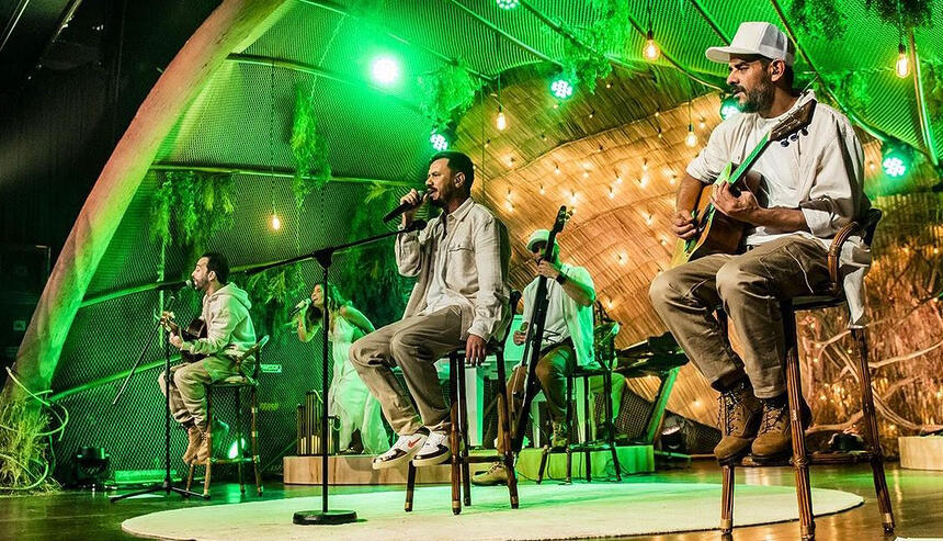 Integrantes da Planta e Raiz sentados, de camisa branca e calça marrom durante gravação do 'Acustico Planta e Raiz'