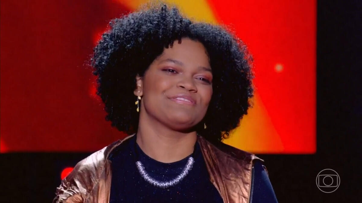 Agatha Henriques com uma roupa preta, no palco do The Voice Brasil