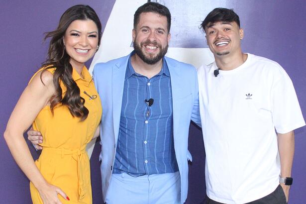 Amanda Françozo de vestido laranja, cabelo solto para o lado direito, sorrindo; Mauricio Meirelles de blazer e calça azul claro, sorrindo, ao lado de Gerson Albuquerque, sorrindo, de camisa branca, chapéu preto durante gravação do Foi Mau, da RedeTV!