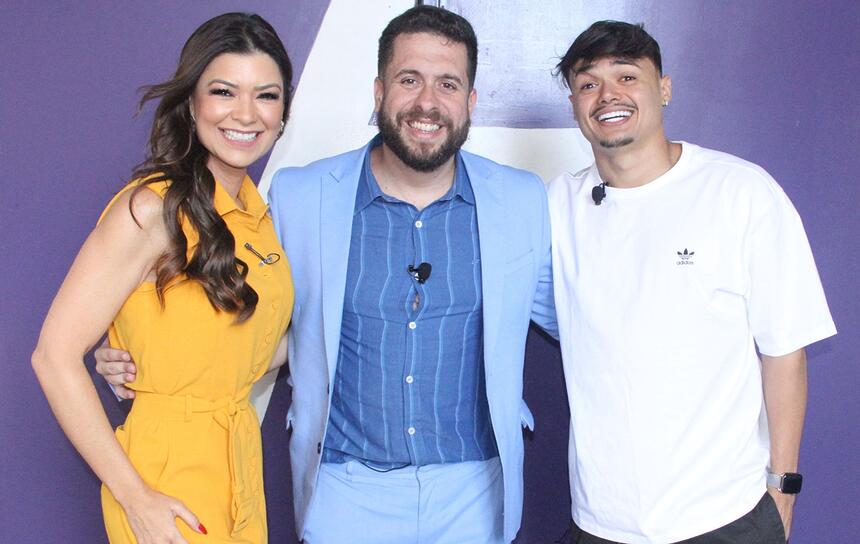 Amanda Françozo de vestido laranja, cabelo solto para o lado direito, sorrindo; Mauricio Meirelles de blazer e calça azul claro, sorrindo, ao lado de Gerson Albuquerque, sorrindo, de camisa branca, chapéu preto durante gravação do Foi Mau, da RedeTV!