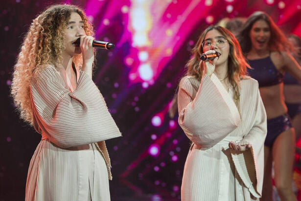 Anavitória com manta bege, segurando microfone durante performance no Faustão na Band