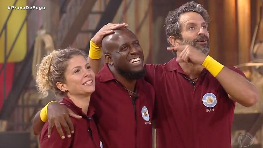 André Marinho sorrindo ao lado de Bárbara Borges e Iran Malfitano, ambos usando a farda da Prova de Fogo de A Fazenda 14, da Record TV