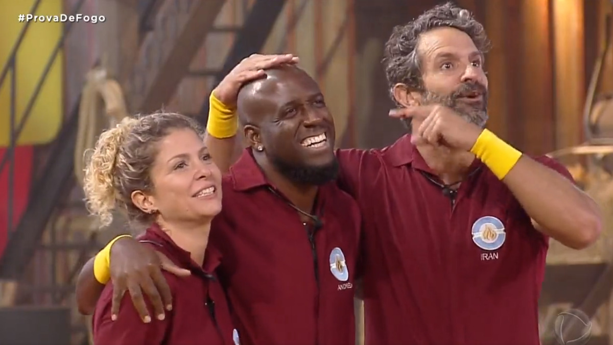 André Marinho sorrindo ao lado de Bárbara Borges e Iran Malfitano, ambos usando a farda da Prova de Fogo de A Fazenda 14, da Record TV