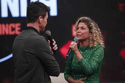 Rodrigo Faro, com casaco preto, se costas para a câmera e de frente para Bárbara Borges, com um vestido verde, no palco e em trecho do programa Hora do faro