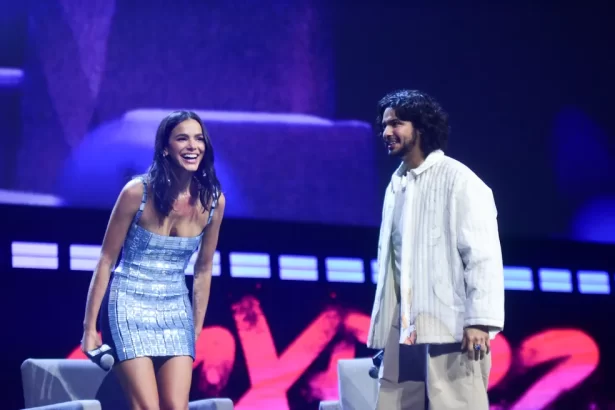 Bruna Marquezine de vestido curto azul claro, sorrindo, de cabelo solto, ao lado de Xolo Maridueña, de jaqueta, camisa e calças brancos, na CCPX 2022