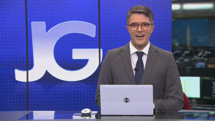 Bruno Tavares, de terno e gravata, sentado na bancada do Jornal da Globo, com o telão ao fundo